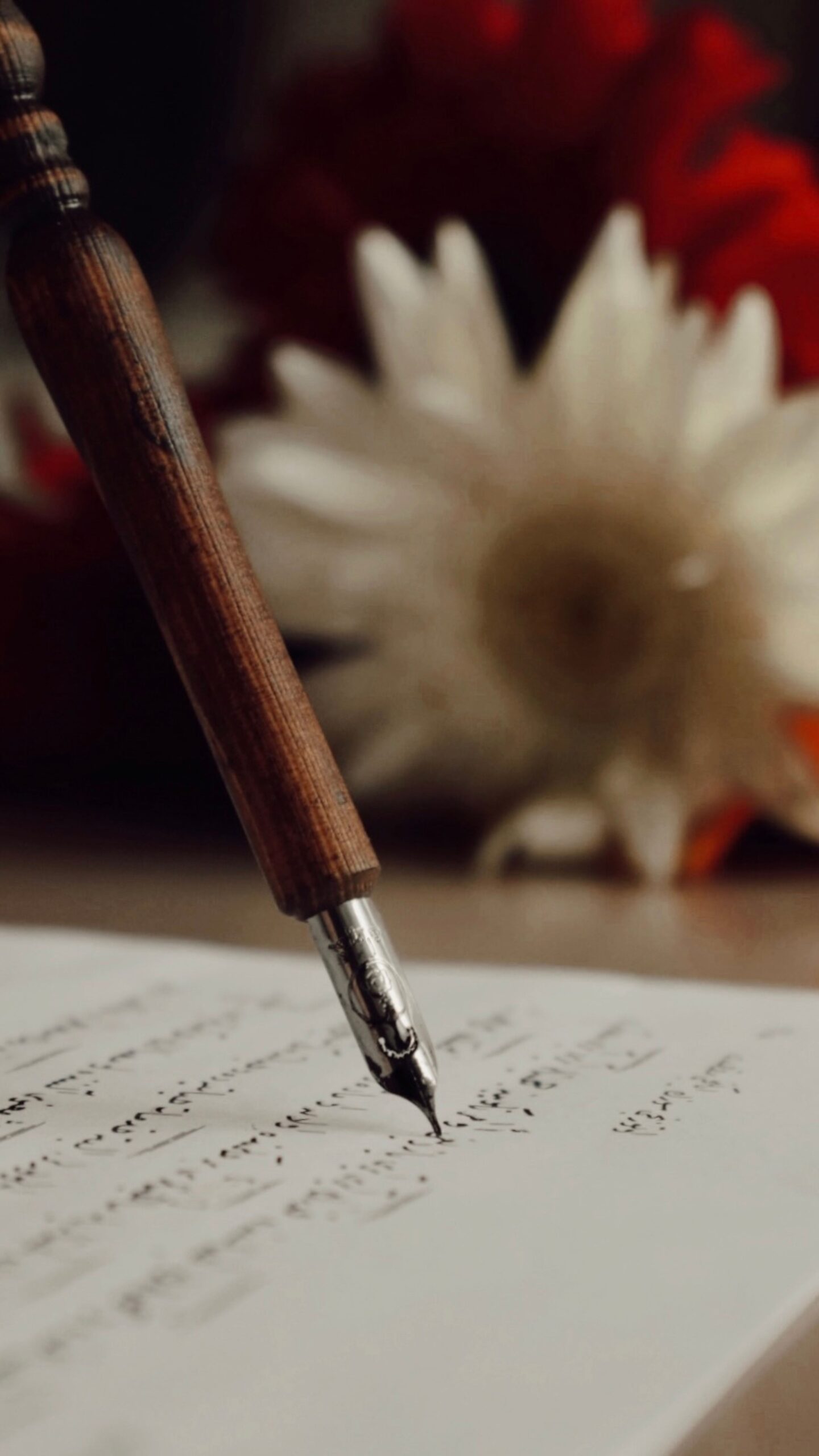 Escritura Close-up of a wooden fountain pen writing calligraphy on paper with blurred flowers in the background.