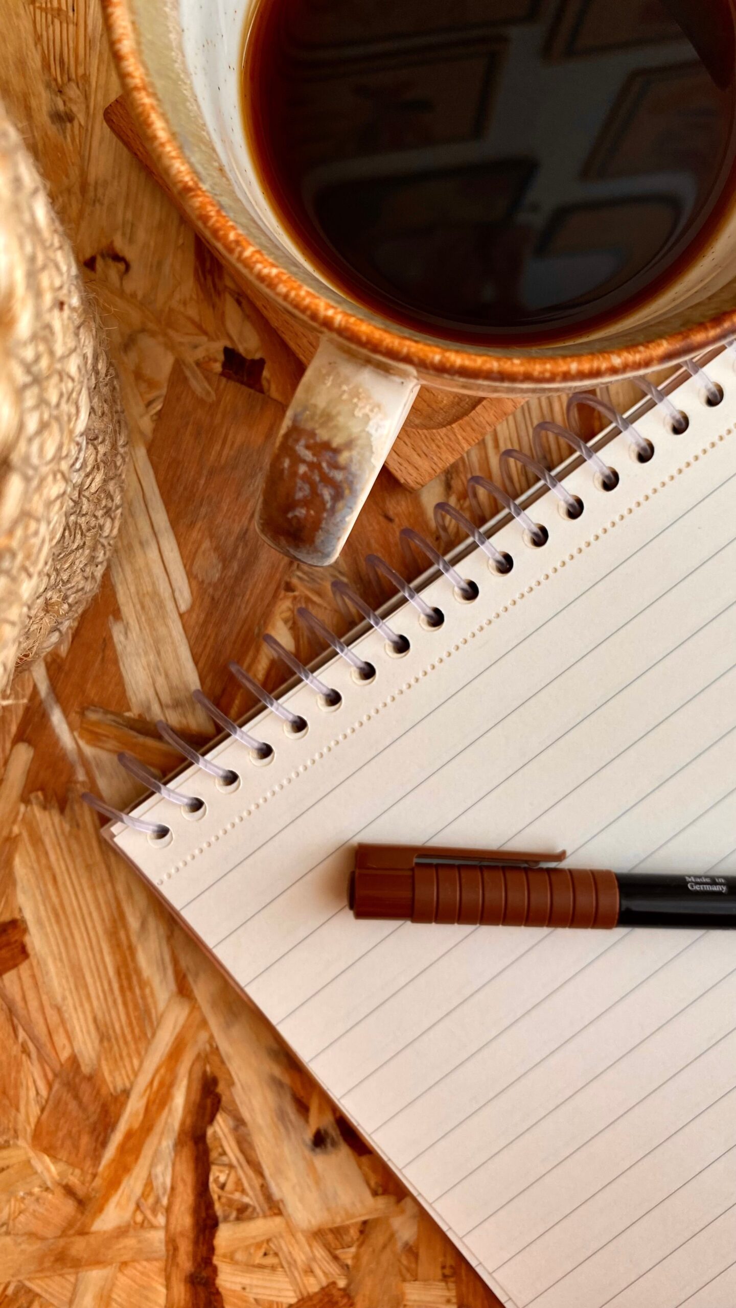 Escritura Top view of a cup of coffee, spiral notebook, and pen on a wooden table.