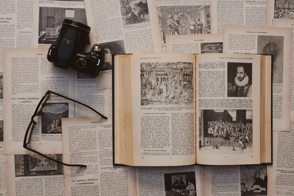 Flat lay of a vintage book, camera, and glasses on historical text pages, evoking nostalgia and learning.