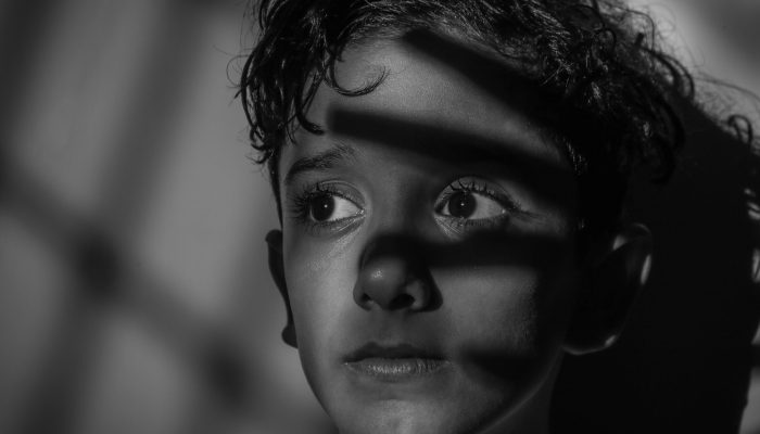 Arresting black and white portrait of a serious child with dramatic shadows.